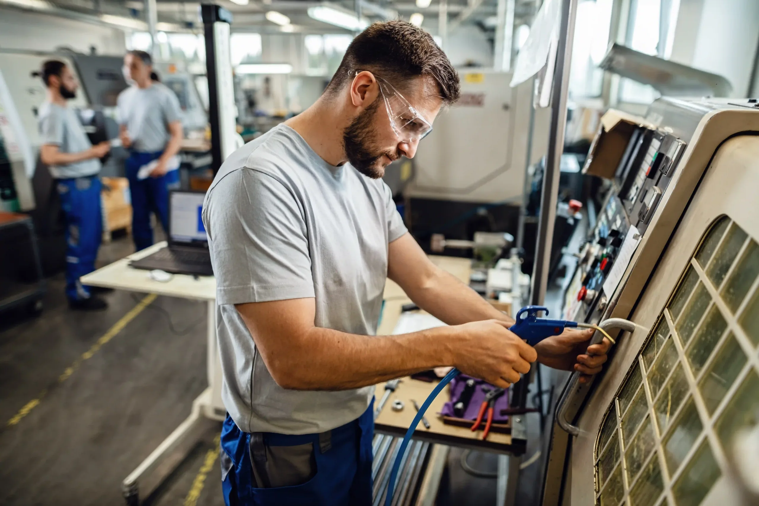 Técnico industrial utilizando pistola de ar comprimido para limpeza ou manutenção de máquina em fábrica.